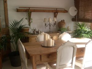 Mesa de comedor de madera con velas, sillas blancas decapadas y candelabro