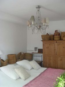 Dormitorio con lámpara de araña, colcha rosa y armario rústico con cestos